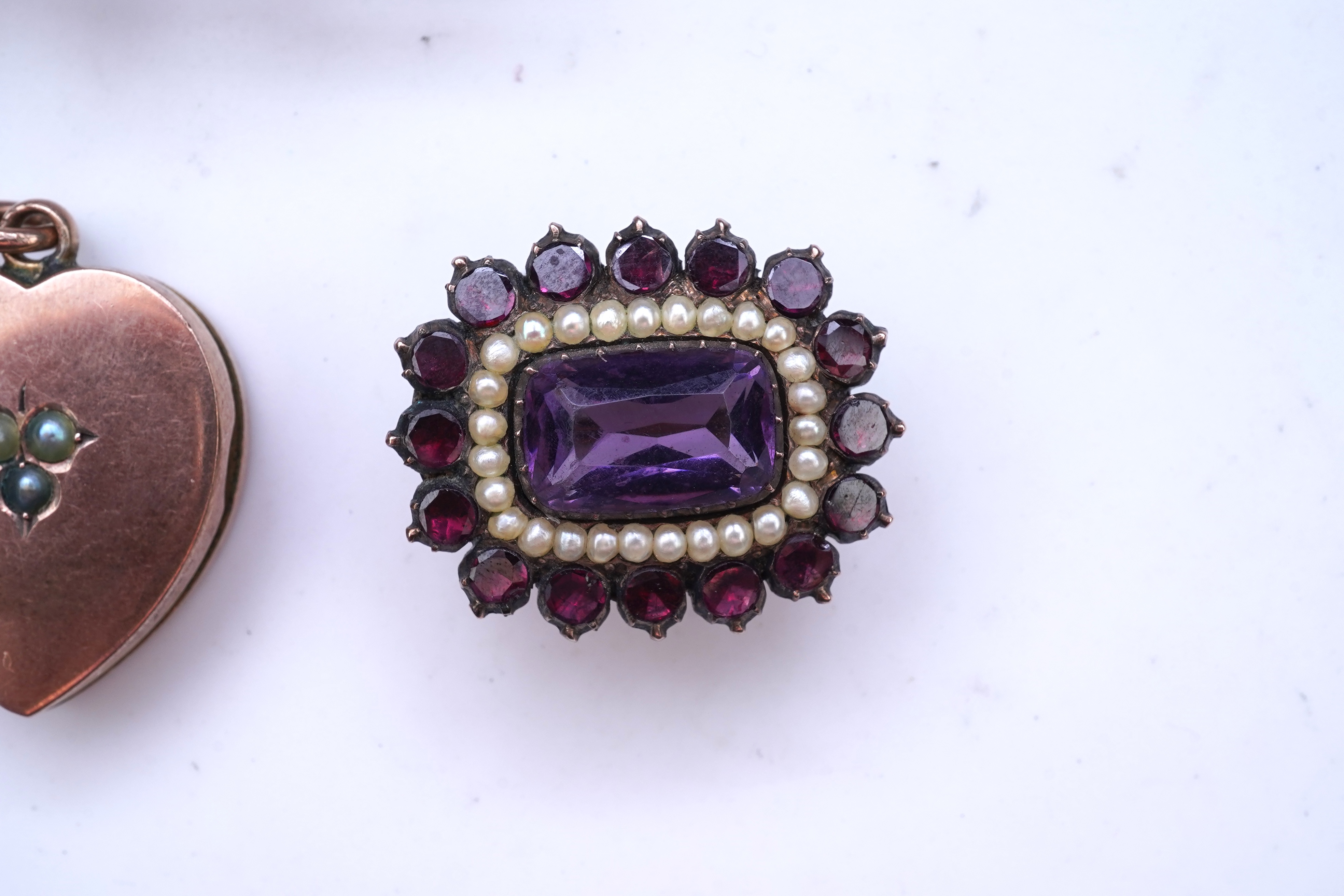 A Victorian yellow metal, amethyst and garnet cluster set brooch, 22mm, an early 20th century yellow metal and seed pearl set heart shaped locket, a yellow metal, garnet and zircon set three stone bar brooch and a tortoi